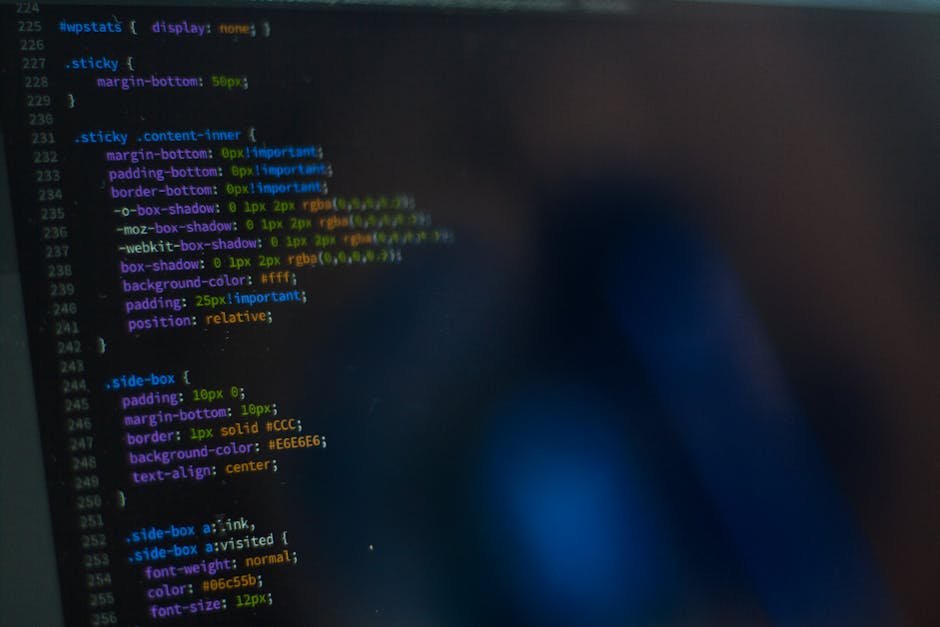 A computer screen displaying a close-up of a code editor with multicoloured lines of HTML and programming language text on a dark background. The code includes tags, attributes, and syntax in red, gre